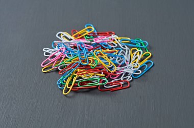 Ofis işi veya eğitim için kırmızı, yeşil, mavi, sarı, beyaz ve pembe renkli ataçlardan oluşan bir yığın koyu renkli beton masa üzerinde uzanıyor. Yakın plan.