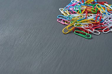 Ofis işi veya eğitim için kırmızı, yeşil, mavi, sarı, beyaz ve pembe renkli ataçlardan oluşan bir yığın koyu renkli beton masa üzerinde uzanıyor. Metin için boşluk