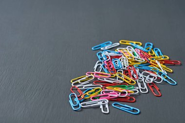 Ofis işi veya eğitim için dağınık renkli ataçlar kırmızı, yeşil, mavi, sarı, beyaz ve pembe koyu renkli beton tablolarda uzanıyor. Metin için boşluk