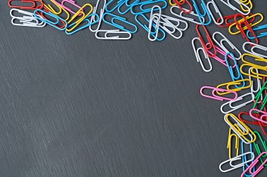 Ofis işi veya eğitim için birçok farklı renkte ataç, kırmızı, yeşil, mavi, sarı, beyaz ve pembe koyu renkli beton masa üzerinde uzanıyor. Mesaj için yer var. Üst görünüm