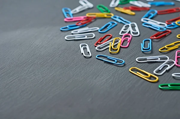 Many scattered different colors paper clips red, green, blue, yellow, white and pink for office work or education lies on dark scratched concrete table. Space for text