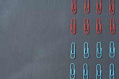 Ofis işi ya da eğitim için kullanılan kırmızı ve mavi renkli ataçların iki bölümü koyu çizik beton masa üzerinde uzanıyor. Mesaj için yer var. Üst görünüm
