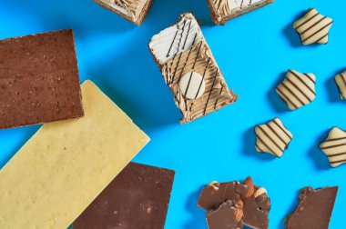 Çikolata çubuğunun yanında dilimlenmiş dikdörtgen pasta ve partide mavi masada duran şekerler. Kutlama konsepti. Yakın plan. Üst görünüm