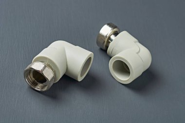 İki polipropilen, 90 derecelik plastik köşeler ve su borularını bağlamak için metal fındık ya da ısıtma odası için diğer sıvılar atölyedeki koyu beton masada yatıyor. Yakın plan.