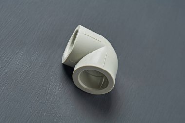 Bir polipropilen, su veya başka bir sıvıyı bağlamak için 90 derecelik plastik bir köşe atölyedeki koyu beton masada yatıyor. Yakın plan.
