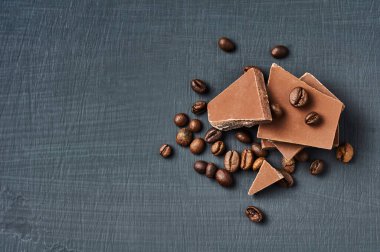 Koyu çizik beton masaya saçılmış kahve çekirdekli acı ya da sütlü çikolata yığını. Mesaj için yer var. Üst görünüm