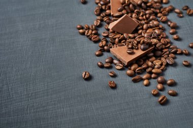Koyu çizik beton masaya saçılmış kahve çekirdekli acı ya da sütlü çikolata yığını. Metin için boşluk