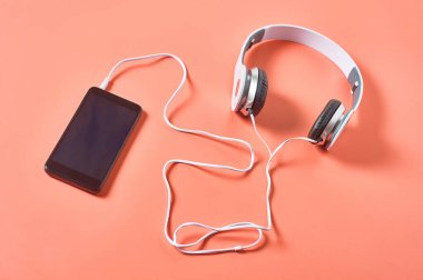 Akıllı telefonun yanında kablo olan modern beyaz kulaklıklar ya da turuncu arka planda tablet. Çağrı merkezi kavramı