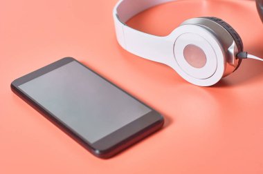 Akıllı telefonun yanında kablo olan modern beyaz kulaklıklar ya da turuncu arka planda tablet. Çağrı merkezi kavramı