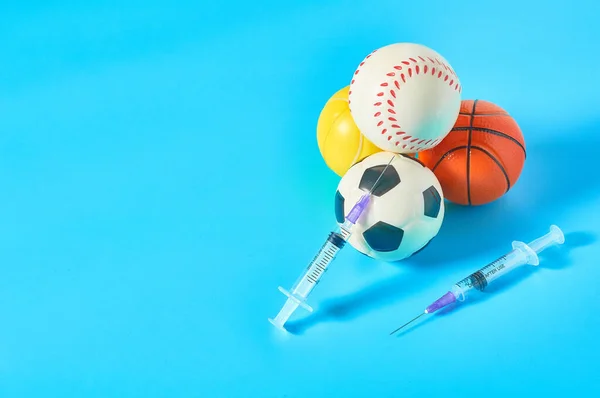 Heap of different balls near syringe on blue background. Concept of doping in professional sport. Rehabilitation, treatment after competition. Illegal medicaments using on tournament