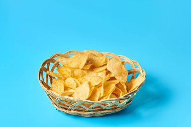 Baharatlı patates cipsi dolu ahşap sepet mavi arka planda. Metin için boşluk
