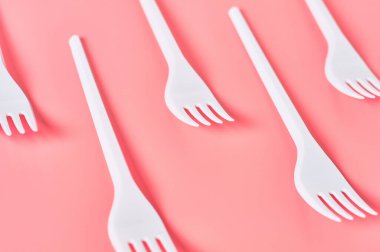 Pembe arka planda tek kullanımlık beyaz plastik çatallar. Piknik, parti ve diğer etkinliklerde tasarruf ortamı, ekoloji, eğlence kavramı