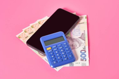 Akıllı telefon, hesap makinesi ve pembe arka planda Ukrayna parası. Mobil bankacılık kavramı. Evden online alışveriş. Uzaklık denetimi mali denge