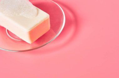 Köpük köpükler ve pembe arka planda cam tabakta bir kalıp sabun. Temizlik, çamaşır, el dezenfeksiyonu kavramı
