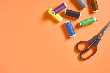 Atölyedeki turuncu terzi masasında renkli iplik ve iğnelerle aksesuar, makas ve makaralar dikmek. Mesaj için yer var. Üst görünüm