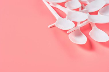 Pembe arka plana saçılmış bir yığın tek kullanımlık kaşık. Çevreyi, ekolojiyi, piknik, parti ve diğer etkinlikleri kurtarma kavramı. Boşluğu kopyala