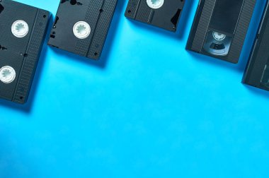 Bir sürü eski siyah plastik video kaset mavi masanın üzerinde boş not defterinin yanında duruyor. 90 'ların konsepti. Uzayı kopyala Üst görünüm