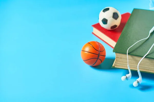 White headphone and old books, toy soccer, football , basketball ball on blue background. Audiobook concept. Online education. E-learning. Modern technology