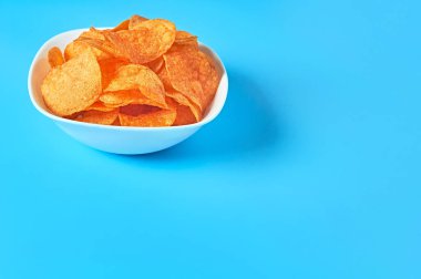 Mavi arka planda patates cipsi dolu beyaz seramik bir kase. Metin için boşluk