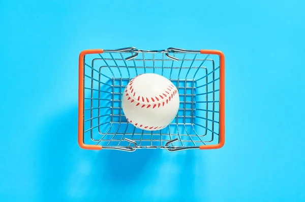 Baseball ball in metal market basket on blue background. Purchasing sport accessories. Concept of corruption in sport