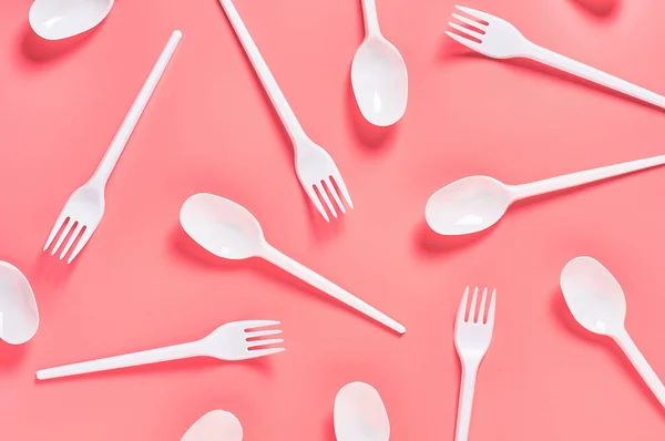 White disposable spoons and forks scattered on pink background. Concept of save environment, ecology, recreation on picnic, party and other events. Top view
