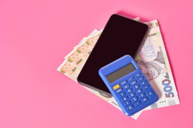 Akıllı telefon, hesap makinesi ve pembe arka planda Ukrayna parası. Mobil bankacılık kavramı. Evden online alışveriş. Uzaklık denetimi mali denge