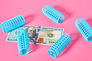 Dağınık plastik silindirik bigudi ve 100 dolarlık banknot güzellik salonundaki pembe masanın üzerine. Kuaför için ödeme ve maliyet. Moda konsepti