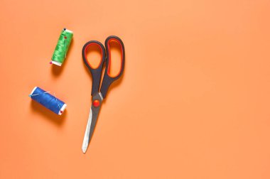 Atölyedeki turuncu terzi masasında renkli iplik ve iğnelerle aksesuar, makas ve makaralar dikmek. Mesaj için yer var. Üst görünüm