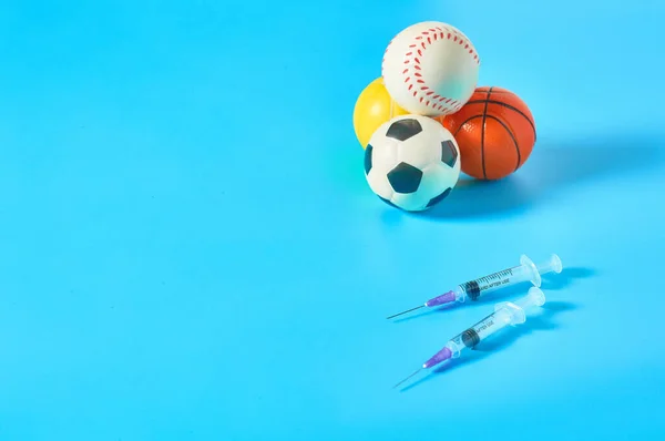 Heap of different balls near syringe on blue background. Concept of doping in professional sport. Rehabilitation, treatment after competition. Illegal medicaments using on tournament