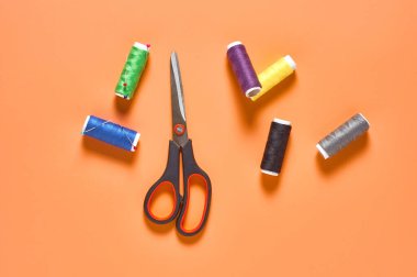 Atölyedeki turuncu terzi masasında renkli iplik ve iğnelerle aksesuar, makas ve makaralar dikmek. Üst Manzara. Yakın plan.