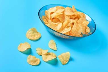 Mavi arka planda bir tabak dolusu patates cipsi. Yakın plan.