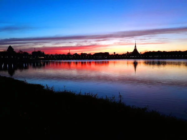 Tayland 'ın Khon Kaen şehrinde, güzel mavi ve turuncu gün ışığı gökyüzünün olduğu göl kenarında gün batımının güzel manzarası. Aynı zamanda ünlü bir tapınağın tapınağını görmek için iyi bir bakış açısıdır.