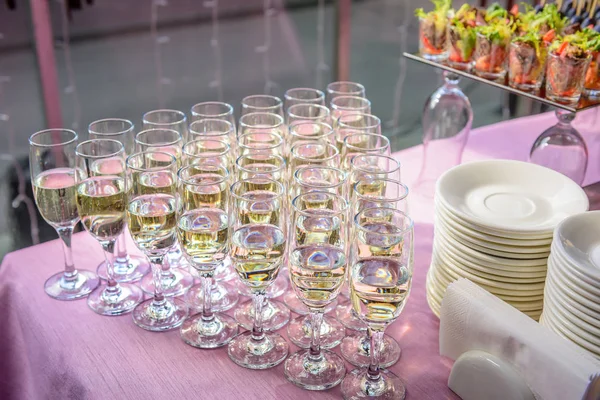 Stuffed glasses with champagne stand in rows on wedding table, close up. Welcome drinks, festive banquet, reception.