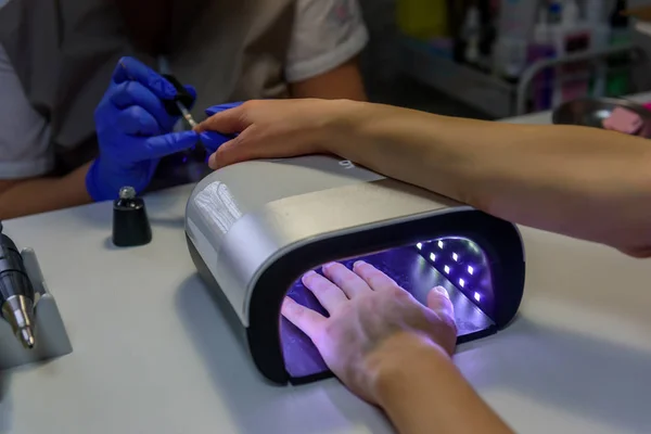 Ultraviolet lamp in manicure salon. Young woman drying nails in lamp. Female hand in UV Gel Acrylic Dryer.