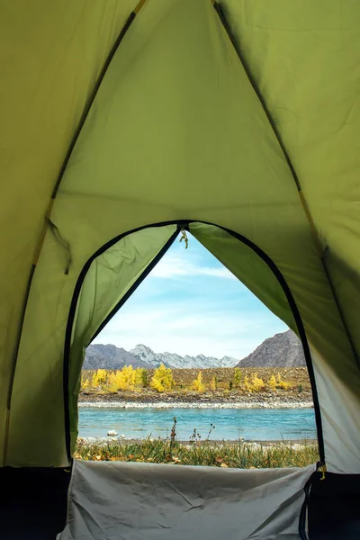 View from the tourist tent on beautiful landscape with turquoise river and high mountains under blue sky. Camping at mountain. Inside the green tent, vertical image with copy space.