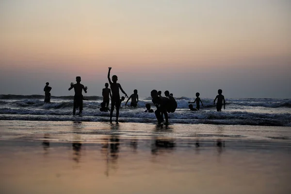 Silhouettes of children jumping in the surf on the background of the sea and evening sky. Boyish figures, children playing on seashore. Carefree childhood, concepts of freedom and the future.