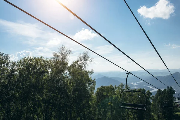 Lift in the mountains on sunny day. Mountain valley with cable car, view from top. Green vegetation in the Altai mountains. Concept of summer vacation.