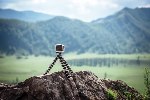 Action camera stands on a portable tripod on a stone close-up. Video camera captures a timelapse: picturesque mountain landscape on a cloudy summer day.