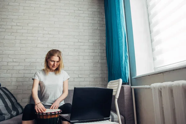 Online music lessons during quarantine due to coronavirus pandemic. Remote teaching to play the drum. Young woman watches video course on playing djembe. Hobbies and leisure activities in lockdown.