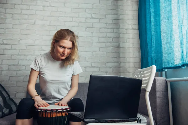 Online music lessons during quarantine due to coronavirus pandemic. Remote teaching to play the drum. Young woman watches video course on playing djembe. Hobbies and leisure activities in lockdown.