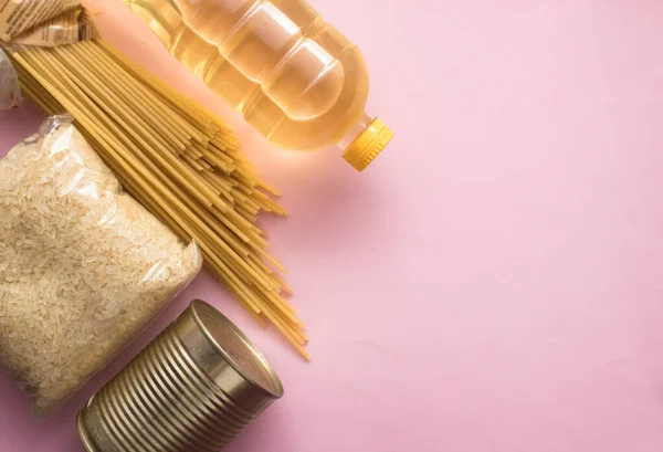 food donation,donation products, rice, vegetable oil, stew, canned food in a tin, spaghetti on a pink background, top view