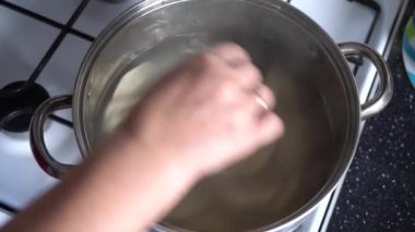 Mutfakta yemek pişirmek için tencerenin yanında bir kadın var.