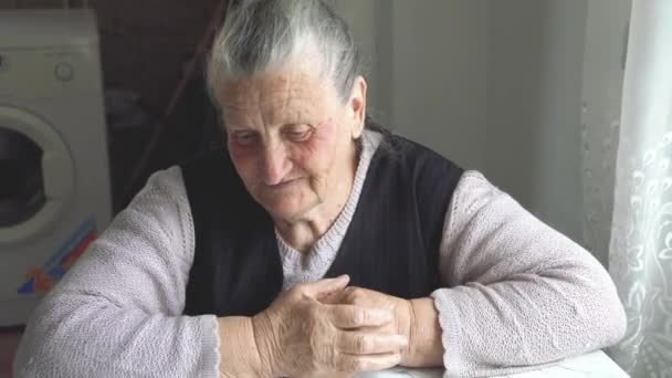 Стара бабуся з прищами на обличчі сидить за столом і розповідає історію — стокове відео