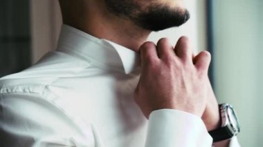 Sakallı bir adam gömlek yakasını düzeltir.