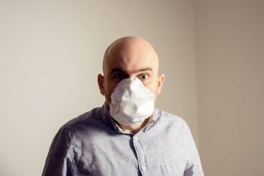 Korkak beyaz adam koruyucu FFP2 antiviral yüz maskesi takıyor.