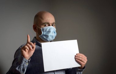 Beyaz, boş bir poster modeliyle koruyucu FFP1 antiviral yüz maskesi takan beyaz dikkat çeken bir adam. işaret parmağı yukarı