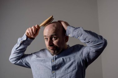 Kafası karışmış, kel bir adam erkek saçlarıyla saç fırçası sorunu yaşıyor.