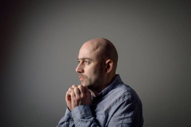 Gri arka planda gri gömlekli, üzgün, kel bir adamın portresi. Yan profil görünümü.