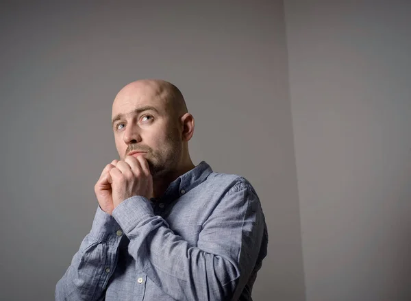 Portrait of caucasian depressed sad bald man in grey shirt on grey background. Side view. Prayer position