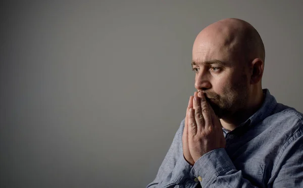 Portrait of caucasian depressed sad bald man in grey shirt on grey background. Side profile view.